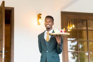 Un uomo in giacca e cravatta che tiene una torta con le candele di Tabebuia Spa and Safari Resort a Fort Portal