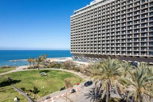 a large building with palm trees in front of the ocean at Hilton Tel Aviv Hotel in Tel Aviv