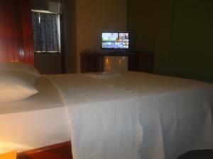 1 dormitorio con 1 cama blanca y TV en el fondo en Pousada Cavaleiros, en Macaé 11 fotos más