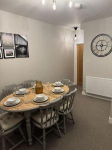 a dining room table with chairs and a clock on the wall at Jasmine Cottage, Newbiggin by the sea in Woodhorn