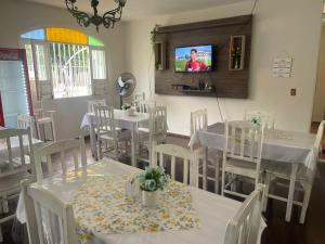 uma sala de jantar com mesas e cadeiras brancas e uma televisão em POUSADA FLOR DO IPÊ em Juazeiro do Norte