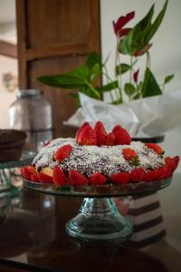 a cake with strawberries on a glass plate on a table at Pousada da Bia in Rio das Ostras