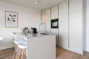 uma cozinha com armários brancos e um balcão com bancos em Veerse Wende em Arnemuiden