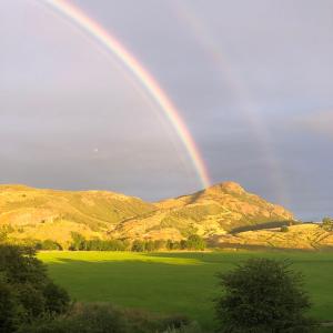 a rainbow in the sky over a green field at Arthur's Seat View in Edinburgh