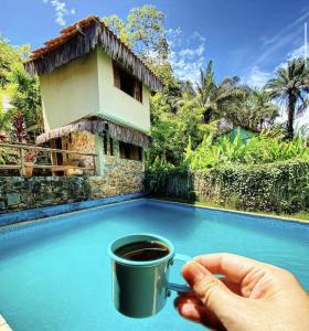 a person holding a cup of coffee in front of a house at Eco Pousada Mentawai in Itacaré