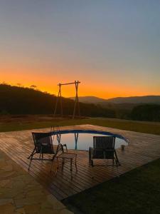 duas cadeiras e uma piscina com o pôr-do-sol ao fundo em Casa vista da serra em São João del Rei