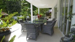 an outdoor patio with a glass table and wicker chairs at Les Jolies Eaux Villa - Chateau Elysium in Beau Vallon