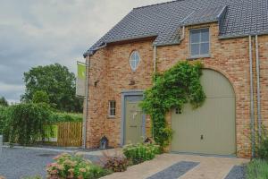 a brick house with a green garage door at De Pluktuin in Kortessem