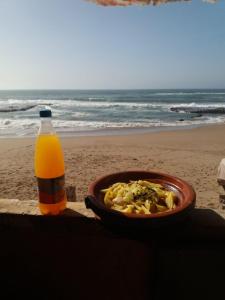 eine Schüssel mit Essen und eine Flasche Orangensaft am Strand in der Unterkunft Raha Cave Said in Douaïra