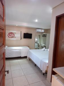 a hotel room with two beds and a tv at Pousada Badejo in Japaratinga