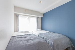 two beds in a blue room with a window at Apartment hotel Hana in Yokohama in Yokohama