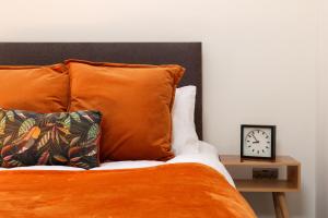 a bed with orange pillows and a clock on a table at Stylish Penthouse with outside balcony! in Bradford