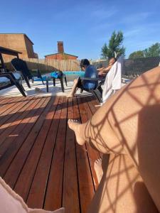 two people sitting on benches on a wooden deck at Casa Vip Pileta Climatizada Carlos Paz in Tanti