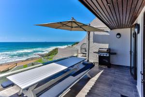 um pátio com uma mesa e um guarda-chuva e o oceano em Chakas Terrace 7 - Luxurious Beach House em Ballito
