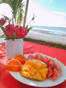 a plate of fruit on a table with a vase with flowers at Palaboy Skatecamp Beach Resort 