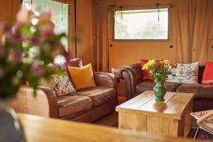 una sala de estar con sofás y un jarrón de flores sobre una mesa en Tall Trees Glamping en Baltonsborough