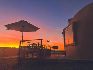 a table with an umbrella and chairs with a sunset in the background at Entre Dunas y Caracolas in Punta de Choros