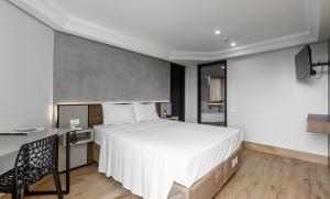 1 dormitorio con 1 cama blanca grande y escritorio en Hotel Portinari Centro, en Foz do Iguaçu