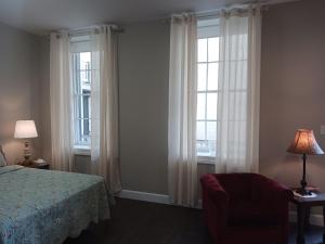 a bedroom with two windows and a bed and a chair at Lee House Inn in Maysville