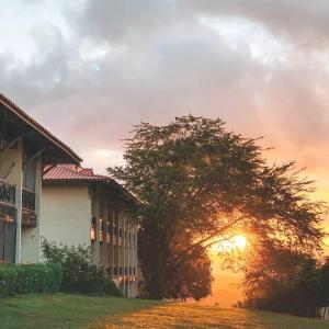 a building and a tree with the sunset in the background at Hotel Fazenda Monte Castelo Flat Gravatá in Bezerros