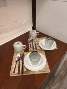 a table with plates and cups and utensils on it at Luxury Cosy Retreat Apt in London