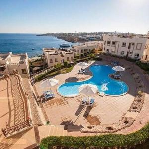 an aerial view of a pool with umbrellas and the ocean at Sharks Bay Oasis Resort & Butterfly Diving Center in Sharm El Sheikh