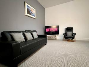 a living room with a black couch and a television at Luxury Victorian House Sleeps 6 - 11 Guests JLR, Trades, Relocations & Hs2 Welcome Wheelchair Accessible Home FREE Faster WIFI & PARKING in Coventry