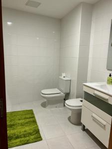 a white bathroom with a toilet and a green rug at Acogedor apartamento ático en el centro de O Porriño in Porriño