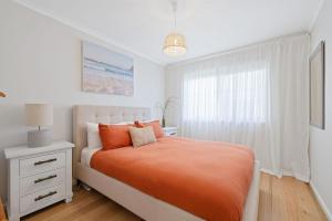 a white bedroom with an orange bed and a window at Salt & Stone in Sunset Strip