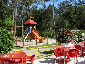 un parque infantil con tobogán y mesas y sillas rojas en Parque de Campismo Orbitur Mira, en Praia de Mira