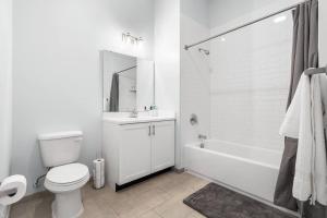 a white bathroom with a toilet and a tub and a sink at Urban Luxury Condo: 20 Mins to NYC (Gym, Laundry) in Jersey City