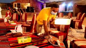 un hombre enmascarado limpiando una mesa en una tienda en Luxury Overnight stay in Desert Safari Campsite, with dinner, adventure, entertainments, and transfers, en Dubái