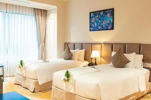 duas camas num quarto de hotel com lençóis brancos em La Vela Hue Hotel em Hue