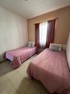 two beds in a room with pink sheets and a window at DEPARTAMENTO PASEOS DE XCACEL in Playa del Carmen