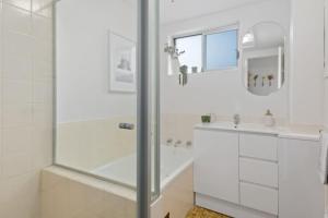 a white bathroom with a shower and a sink at Sea Vista Escape - A Charming Waterside Stay in Wollongong