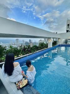 two women sitting next to a swimming pool at ViAn Hotel And Spa Danang in Danang