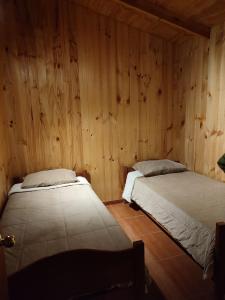 two beds in a room with wooden walls at cabaña de 1 piso in Coñaripe