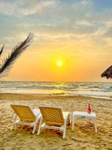 San Silvestre的住宿－Caribbean Escape Lodge，日落时分海滩上的两把椅子和一张桌子