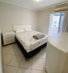 a white bedroom with a bed and a window at Apto à 100m da praia central in Balneário Camboriú