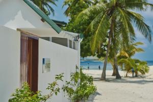 a white building on the beach with palm trees at Akomadoo Retreat in Kamadhoo