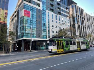 a green and white bus driving down a city street at Essence Hotel Carlton in Melbourne