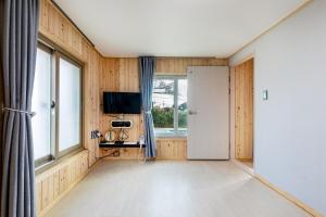 a room with wooden walls and a door and a television at Donnaeko Pension in Seogwipo
