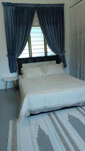 a large bed with blue curtains and a window at Homestay Laman Dahlia in Kuala Kangsar