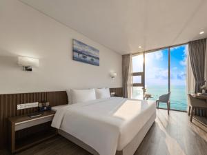 a bedroom with a large white bed and a desk at Mangata Beachfront Hotel in Da Nang
