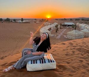 a woman sitting on a bed in the desert at Merzouga luxurious Camp in Merzouga
