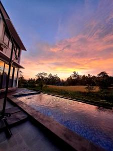 una piscina frente a una casa con puesta de sol en Maple Ridge Ubud Villas, en Ubud