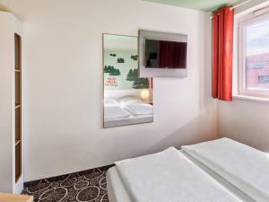 a white room with two beds and a mirror at B&B Hotel Aschaffenburg in Aschaffenburg