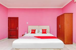a bedroom with pink walls and a bed with red pillows at OYO 90218 Ubaran Guest House in Bandung