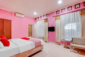 a bedroom with pink walls and a bed and a chair at OYO 90218 Ubaran Guest House in Bandung