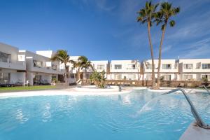 a swimming pool with palm trees in front of a building at Hotel Siroco - Adults Only 18 in Costa Teguise